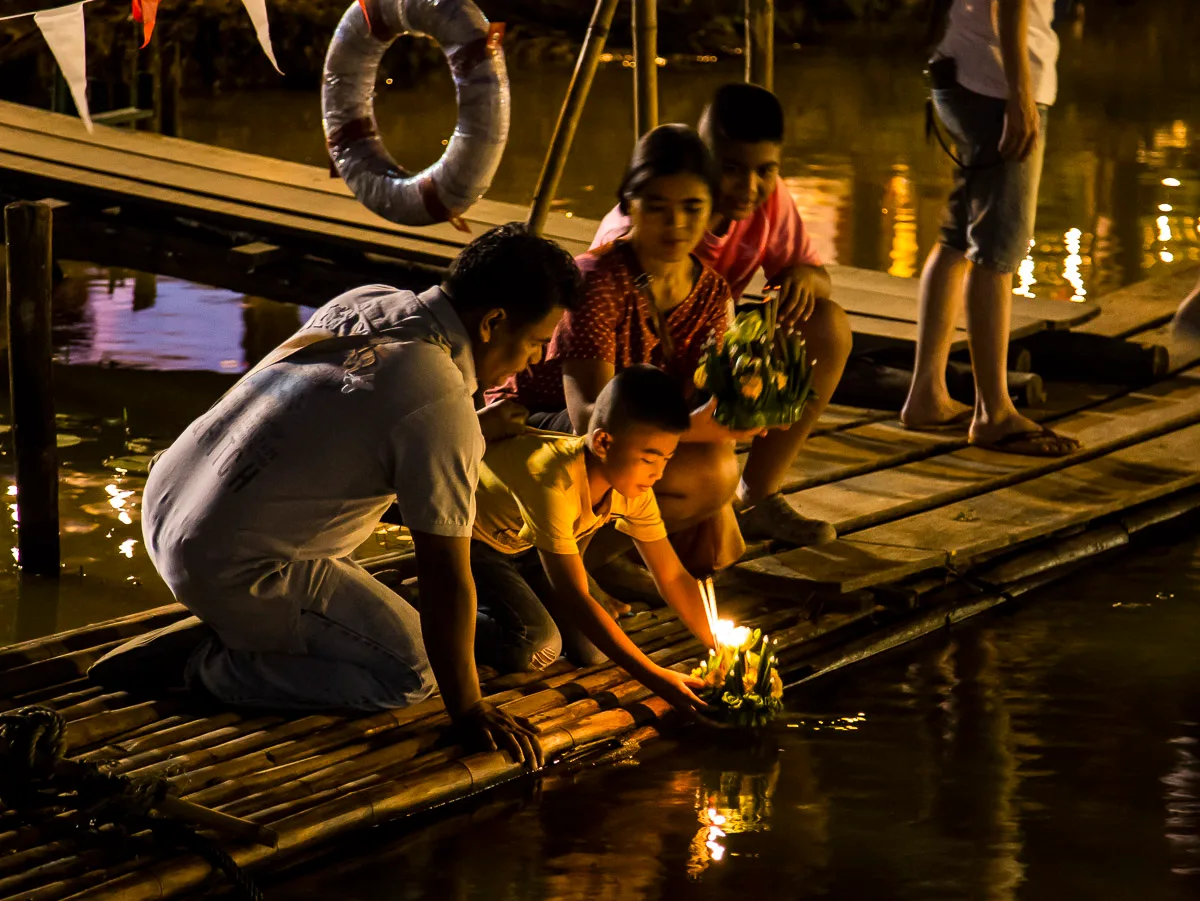 Thai family floating a candle-lit krathong from a bamboo jetty on the Ping River in Chiang Mai