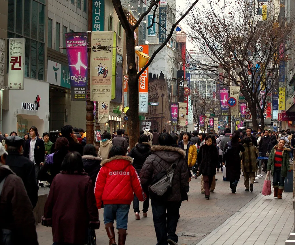 Crowds fill Myeongdong's main shopping street, with bank and retail signage lining the buildings overhead. — Photo: by thelearnr (CC BY 2.0)