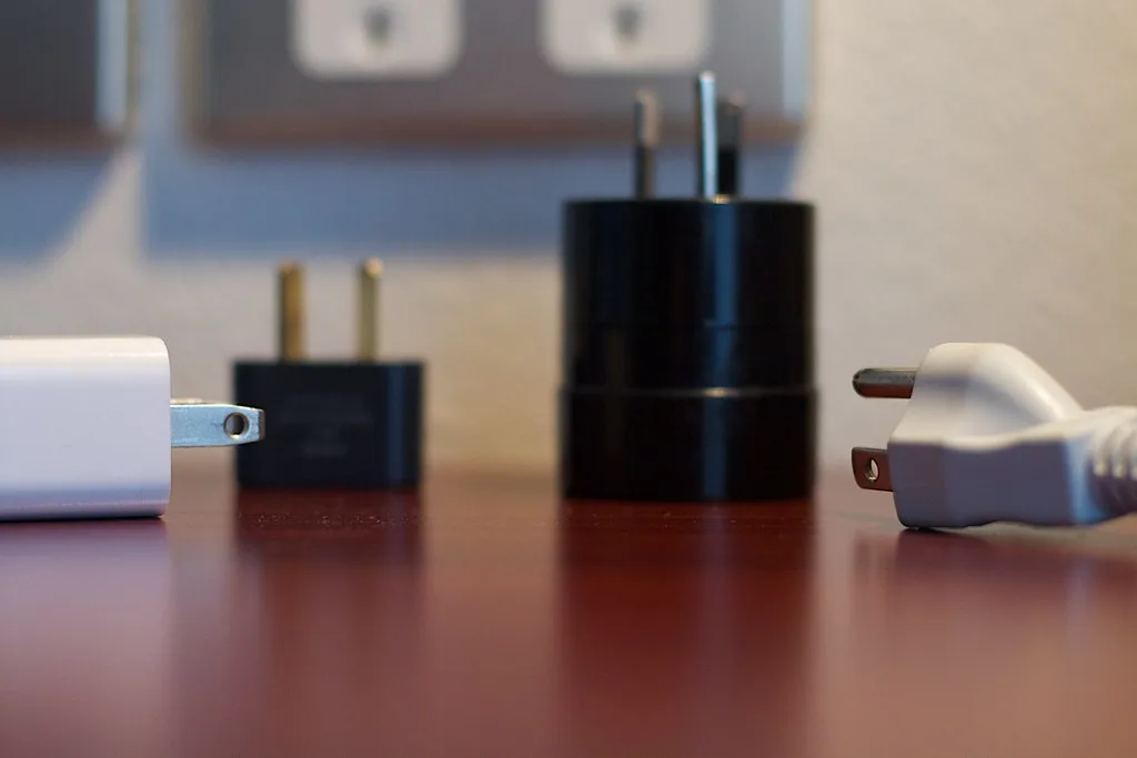 Travel plug adapters lined up in front of flat-blade Type A wall outlets — Photo: cogdogblog (CC BY 2.0)